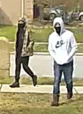 Photo of two suspects. One suspect is dressed in black with a camo hoodie. Second suspect is wearing boots, jeans, and white Nike hoodie. Both suspects are masked. 